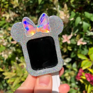May include: A silver glitter watch case with a holographic bow, designed to look like Minnie Mouse's ears.