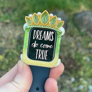May include: A green and yellow watch band with a crown design and glitter accents. The watch face has the text "DREAMS do come TRUE".