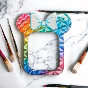 May include: A rainbow-colored phone case with a white bow and a geometric pattern. The case is designed to look like Mickey Mouse ears.