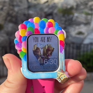 Op de afbeelding: Een roze Apple Watch met een witte wijzerplaat en een transparante behuizing met een hartvormig beeld van de personages uit de film Up. De behuizing is versierd met kleurrijke ballonnen en de tekst "You are my greatest adventure" staat op de wijzerplaat. De tijd die op de wijzerplaat wordt weergegeven is 6:30 en de datum is "Wed 19".