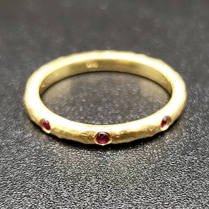 May include: A gold band ring with a hammered texture and five small red gemstones set into the band.