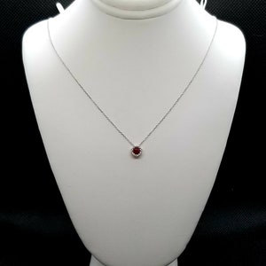 May include: A silver chain necklace with a small red gemstone pendant surrounded by a halo of smaller white gemstones.