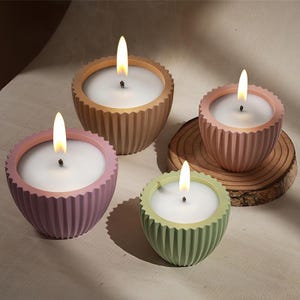 Op de afbeelding: Vier kaarsen in verschillende kleuren, elk met een geribbeld ontwerp en een witte was bovenkant. De kaarsen zijn aangestoken en de vlammen zijn zichtbaar.