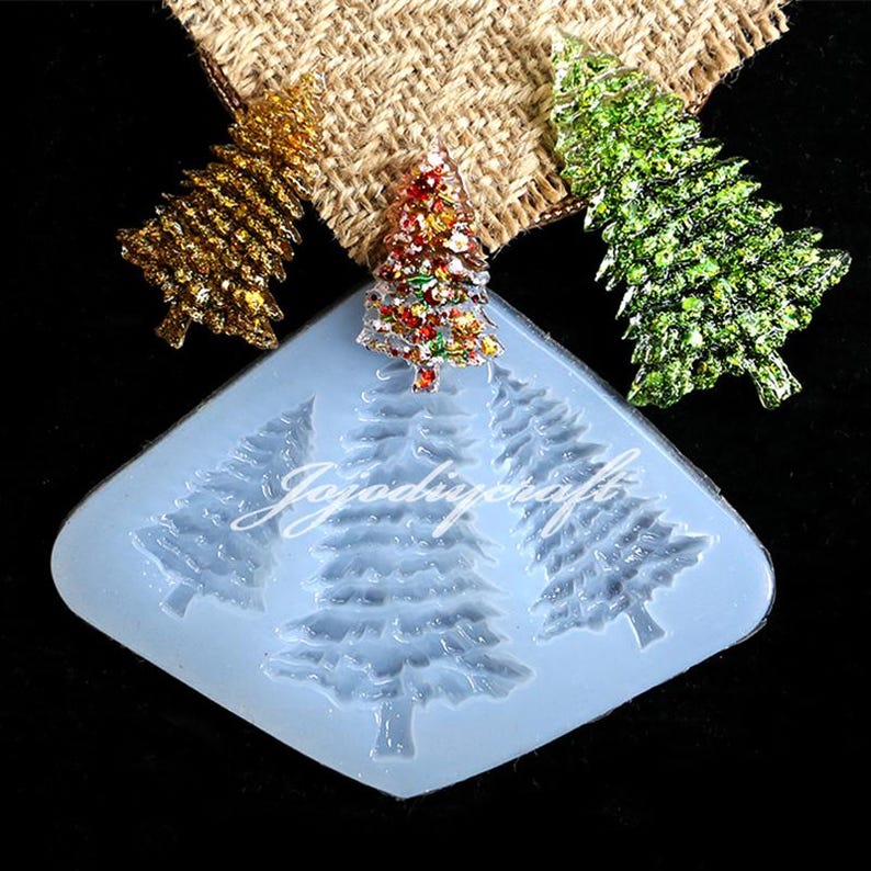 May include: A blue silicone mold with three Christmas tree shapes. The mold is designed to create resin ornaments. Three glitter-covered Christmas trees are shown next to the mold.