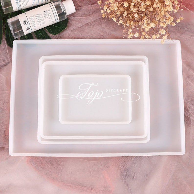 May include: Three white silicone trays of different sizes, nested inside each other. The trays are rectangular and have smooth, rounded edges. The largest tray is about 10 inches long and 7 inches wide.