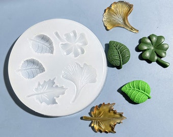 Puede incluir: Un molde de silicona blanco con siete formas de hojas. El molde está lleno de hojas de resina verde y amarilla.