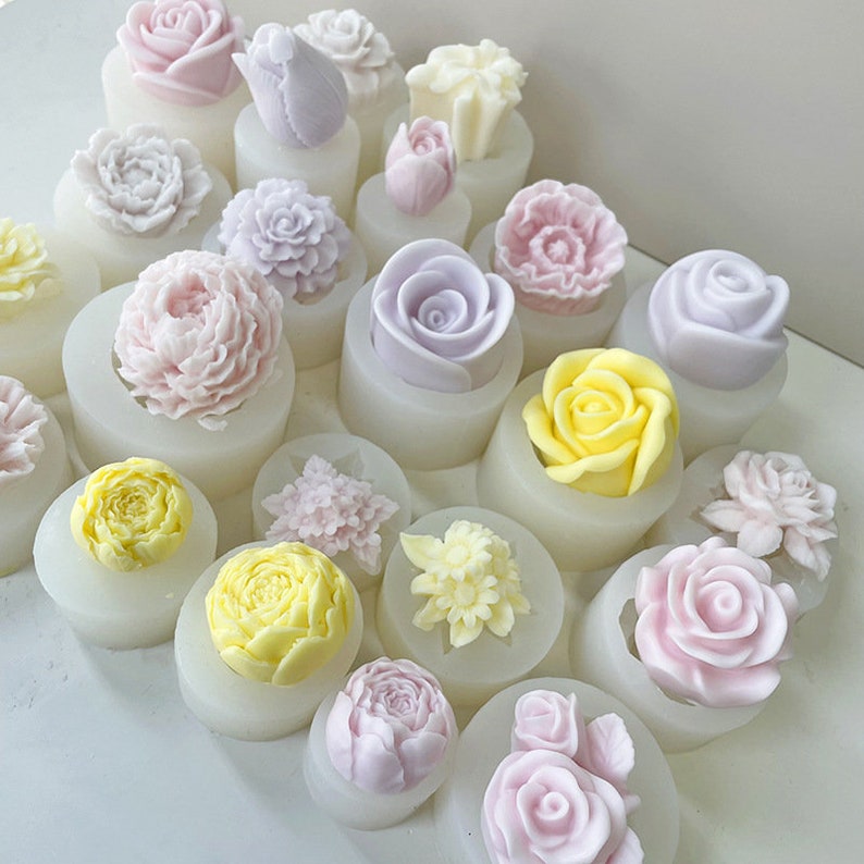 May include: A set of 18 silicone molds for making flower-shaped candles or soap. The molds are white and feature a variety of flower designs in pink, purple, and yellow.