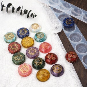 May include: A set of 12 chakra stones, each with a different color and symbol. The stones are arranged in a circle on a white surface. The stones are used for healing and meditation.