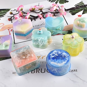 May include: Assortment of colorful resin boxes with various shapes, including a heart, a flower, a hexagon, and a square. The boxes are decorated with glitter, pearls, and gold lettering. The boxes are perfect for storing small trinkets or jewelry.