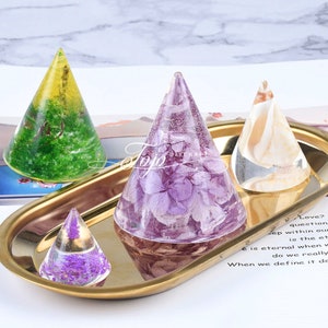 May include: Four clear resin cone-shaped ornaments with different dried flower and leaf inclusions. The cones are displayed on a gold tray.