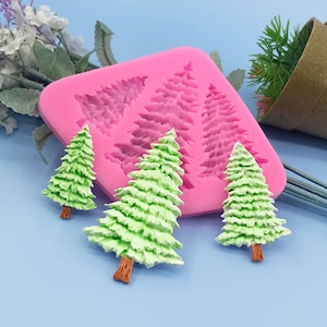 May include: Pink silicone mould with four different sized Christmas tree shapes. Three green Christmas trees are shown outside of the mould.