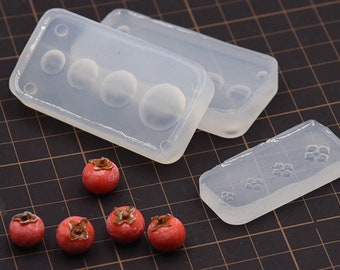 Puede incluir: Tres moldes de silicona transparentes para hacer fruta roja en miniatura. Los moldes son rectangulares y tienen diferentes formas. Hay seis frutas rojas en miniatura junto a los moldes.