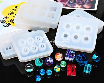 May include: A set of clear silicone molds for making resin crafts. The molds are in different shapes, including circles, squares, and rectangles. There are also several small resin pieces in various colors and shapes, including spheres, cubes, and flowers.