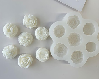 May include: White silicone mold with eight flower-shaped cavities. The mold is on a white surface with eight white flower-shaped decorations.