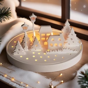 May include: White wooden Christmas village scene with a round base and cut-out houses, trees, and streetlights. The base has small holes that allow light to shine through, creating a warm glow.