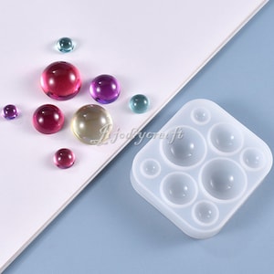 May include: A white silicone mold with six round cavities for making resin jewelry. The mold is shown with several colorful resin cabochons.