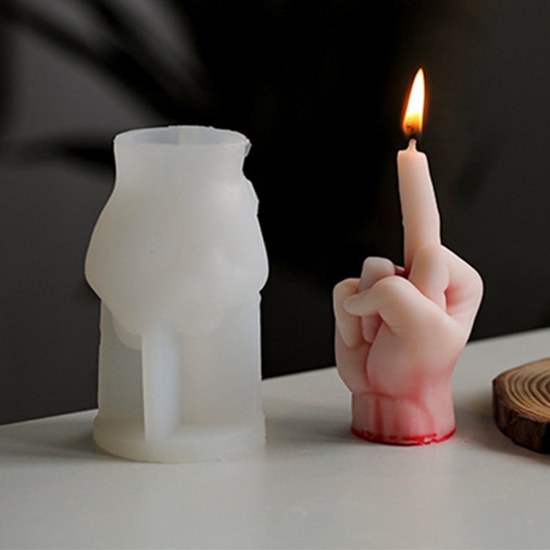 Pu&ograve; includere: Uno stampo in silicone bianco a forma di mano che fa il dito medio. Accanto ad esso c'&egrave; una candela accesa a forma di mano che fa il dito medio. La candela &egrave; di colore rosa chiaro con accenti rossi.