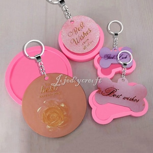 May include: Three pink silicone moulds for making resin keyrings. The moulds are shaped like a circle, a bone, and a bone with a smaller circle inside. The circle mould has a design that says "The best is yet to come" with a rose inside. The bone mould has a design that says "Best wishes". The smaller circle inside the bone mould has a design that says "Good Luck".