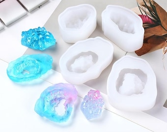 Puede incluir: Cuatro moldes de silicona blancos para hacer manualidades de geodas de resina. Los moldes tienen forma de rocas irregulares, planas, con un centro hueco. También hay cinco piezas de geoda de resina terminadas en varios tonos de azul y rosa.