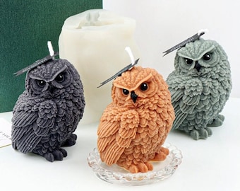 May include: Three owl-shaped candles, one gray, one brown, and one green, with a white candle mold in the background. The candles are handmade and have detailed feather patterns.