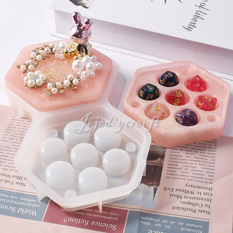 May include: A hexagonal resin mold set with a pink lid featuring a bunny figurine and pearl accents. The set includes a mold for dice and a mold for round objects. The dice are in various colors.
