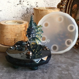 Könnte beinhalten: Ein dunkelblaugrüner Räucherstäbchenhalter aus Kunstharz mit einem baumartigen Design, umgeben von kleinen goldfarbenen Kugeln. Eine transparente Silikonform und ein Kerzenhalter aus Birkenholz sind ebenfalls sichtbar. Der Text "Tojoyusarft" befindet sich auf dem Räucherstäbchenhalter.