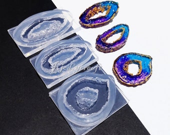 May include: Four clear silicone molds for making resin agate slices. The molds are rectangular with a rounded oval shape in the center. Three finished resin agate slices are shown in the image. The slices are iridescent with blue, purple, and gold glitter.