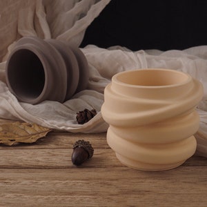 May include: Two ceramic planters with a unique swirl design. The planter on the left is grey and the planter on the right is light beige.