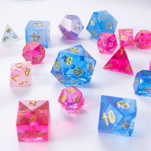 May include: A set of 12-sided dice in blue, pink, and purple with gold numbers. The dice are made of clear plastic and have a sparkly finish.