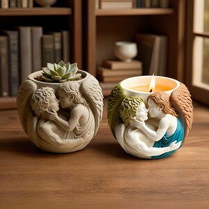 May include: Two round containers featuring sculpted figures of two embracing winged beings. The left container is a monochromatic beige planter holding a succulent. The right container is a multi-colored candle holder with a lit flame and painted details.