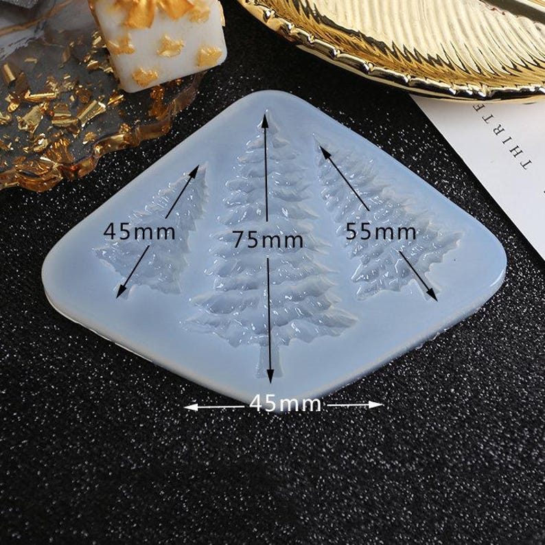 May include: A white silicone mold with three Christmas tree shapes. The mold measures 45 mm by 75 mm by 55 mm.