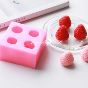 May include: Pink silicone mould with four cavities shaped like strawberries.  Four red strawberry-shaped sweets are shown on a clear glass plate.