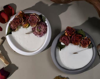 Puede incluir: Dos portavelas redondos, blanco y gris, con rosas secas y una mecha en el centro. Las velas son blancas y los portavelas están hechos de un material texturizado.