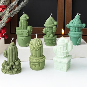 May include: Six green and white cactus-shaped candles. The candles have different designs, including a Santa hat, a snowman, and a reindeer. One candle has the text "Merry Christmas" on a sign.