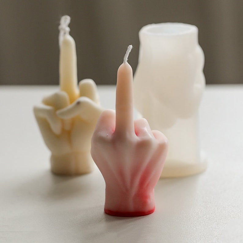 Pu&ograve; includere: Tre candele a forma di mano, bianche e rosa. Le candele hanno la forma di un dito medio.