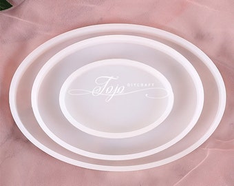 Può includere: Tre stampi in silicone ovali bianchi per la colata di resina. Gli stampi sono annidati uno dentro l'altro, con lo stampo più grande in basso e quello più piccolo in alto. Gli stampi sono su uno sfondo di tessuto rosa. Il testo "Jojo DIYCRAFT" è stampato sullo stampo più grande.