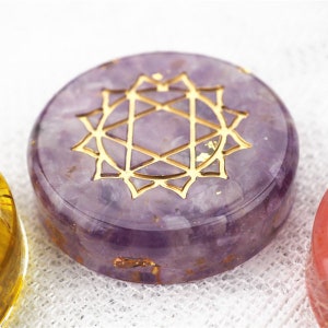 May include: A round, purple amethyst crystal with a gold geometric design on top. The crystal is used for chakra healing and meditation.