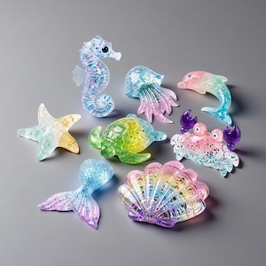 Könnte beinhalten: Eine Sammlung farbenfroher, glitzergefüllter Meeresfiguren. Enthält ein Seepferdchen, eine Qualle, einen Delfin, einen Seestern, eine Schildkröte, eine Krabbe, eine Meerjungfrauenflosse und eine Muschel. Die Figuren sind in Blau-, Grün-, Rosa- und Gelbtönen mit schillerndem Glitzer gehalten.