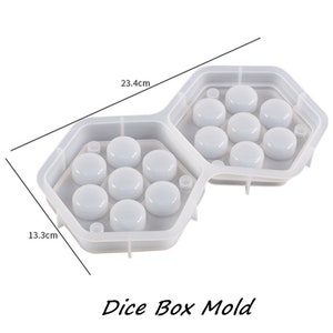 May include: A clear, hexagonal dice box mold with two connected compartments, each holding seven circular impressions. The mold measures 9.2 inches long and 5.2 inches wide. The text "Dice Box Mold" is at the bottom.