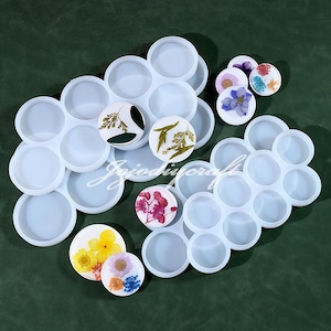 May include: Two sets of white silicone molds for making resin crafts. Each mold has multiple circular cavities of varying sizes. The molds are shown with dried flowers in some of the cavities.