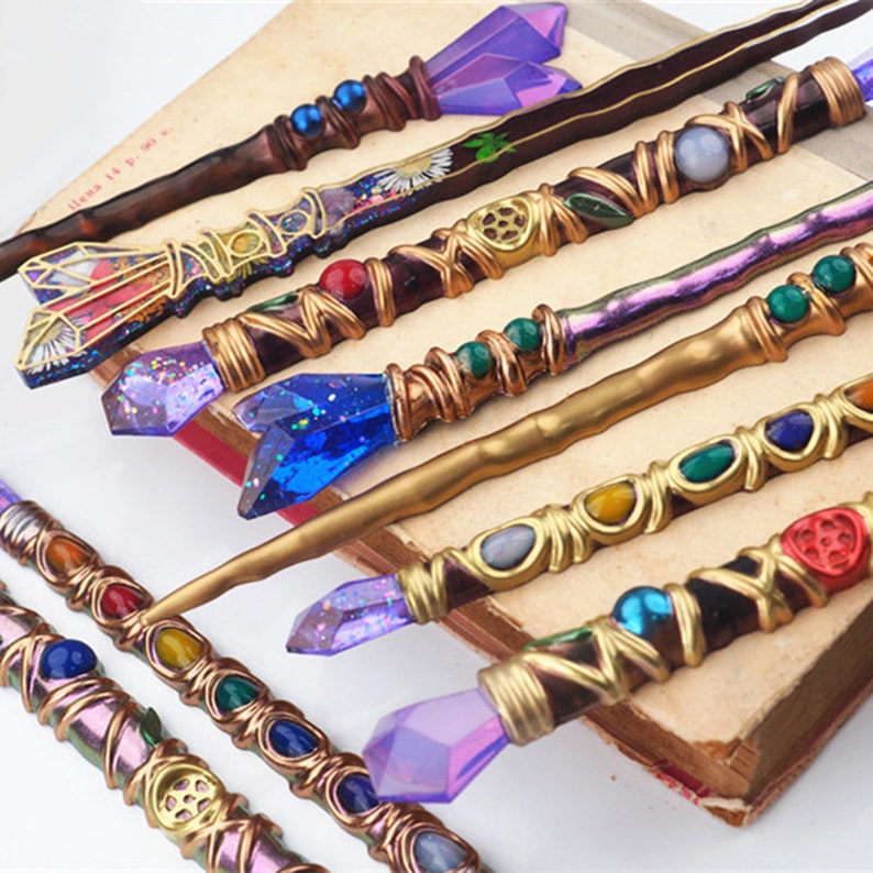 Puede incluir: Una colecci&oacute;n de ocho varitas decorativas con cristales y cuentas de varios colores. Las varitas est&aacute;n hechas de madera y tienen un alambre de cobre envuelto alrededor. Las varitas est&aacute;n dispuestas sobre un libro con una cubierta marr&oacute;n.