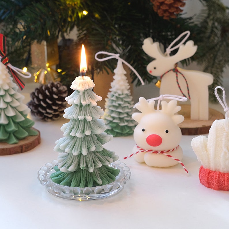 May include: A set of Christmas-themed candles, including a green and white tree candle, a white reindeer candle, and a white snowman candle. The candles are all hand-crafted and have a rustic, vintage look.