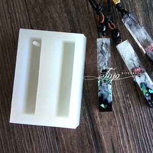 Peut inclure: Un moule en silicone blanc avec deux cavités rectangulaires pour la fabrication de pendentifs en résine. Le moule a un petit trou en haut de chaque cavité pour ajouter une bélière.