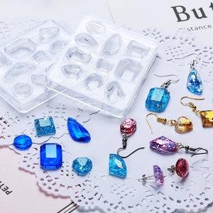 May include: A clear plastic mold with 12 different shaped cavities for making jewelry. The mold is next to a variety of colorful resin earrings, including blue, pink, purple, and gold.