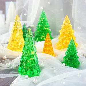 Könnte beinhalten: Ein Set mit sechs gläsernen Weihnachtsbaumschmuck, mit drei grünen und drei gelben Bäumen. Der Schmuck ist aus klarem Glas mit einer strukturierten Oberfläche und hat kleine Lichter im Inneren.