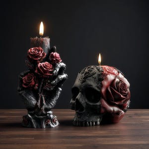 Könnte beinhalten: Zwei gotische Kerzen. Eine ist ein schwarzer Schädel mit einer roten Rose, die andere ist eine schwarze Hand, die rote Rosen hält. Beide Kerzen haben brennende Flammen, vor dunklem Hintergrund auf einer Holzoberfläche.