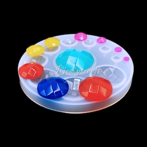 May include: A white silicone mold with 10 round cavities for making resin jewelry. The mold is filled with colorful resin cabochons in various shades of blue, red, yellow, and pink.