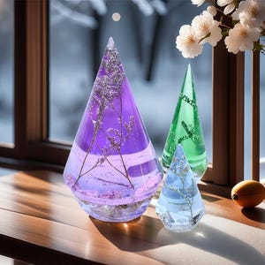 Può includere: Tre ornamenti di vetro a forma di cono, ognuno riempito di fiori secchi e sigillato con resina. L'ornamento più grande è viola, l'ornamento intermedio è verde e l'ornamento più piccolo è blu.