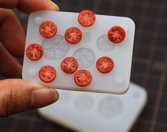 May include: A white silicone mold with nine round cavities, each filled with a red tomato slice. The mold is on a white surface.