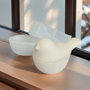 Peut inclure: Un récipient en céramique blanche en forme d'oiseau avec un couvercle amovible. Le récipient est fait d'une finition lisse et mate.